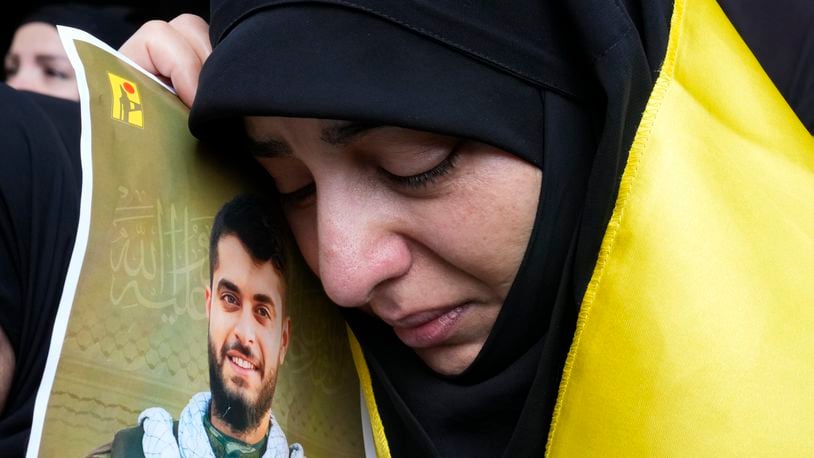 A woman holds a picture of a Hezbollah member who was killed on Wednesday when a handheld device exploded, during his funeral procession in the southern suburbs of Beirut, Thursday, Sept. 19, 2024. (AP Photo/Hussein Malla)