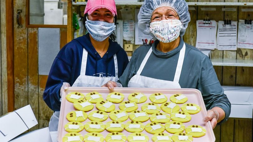 Alyssa Hyden, left, and owner Vera Slamka show off a tray of cookies with masks on them Monday, April 13, 2020 at Central Pastry in Middletown. Central Pastry has taken several steps to maintain safety of employees and customers. They are wearing face masks and gloves, have installed shields in front of the counters and have assigned spaces on the floor to keep customers spaced out during busy times in the shop. NICK GRAHAM / STAFF