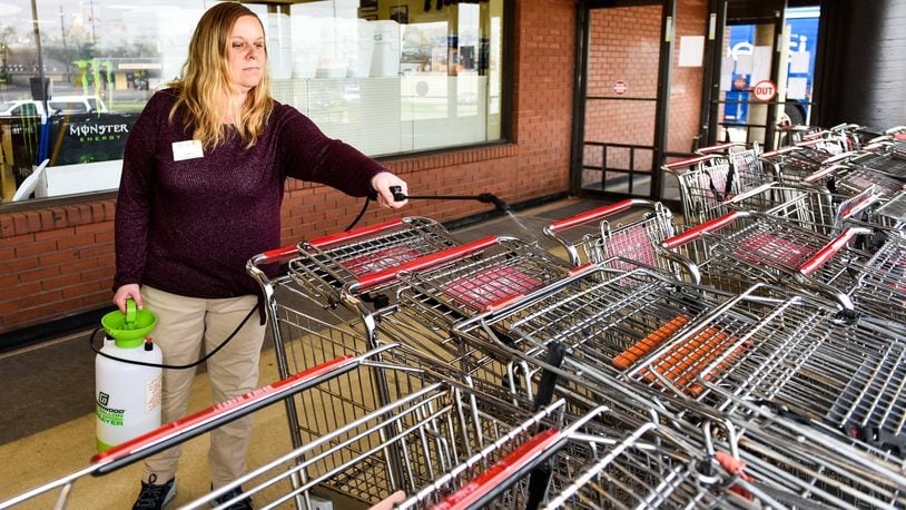 Lauren Schuerman, a manager at Needler’s Fresh Market, on N. University Blvd. in Middletown sprays sanitizer on carts at the entrance Tuesday morning, April 7, 2020. A sign on the door says a maximum of 117 customers are allowed in the store at a time. NICK GRAHAM/STAFF
