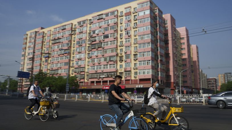 Chinese riding bicycle pass by a local business building the in background in Beijing, China, Friday, June 28, 2024. Surveys of Chinese factory managers showed a mixed outlook for the world's second-largest economy in June, with growth steady but not picking up much steam. (AP Photo/Vincent Thian)
