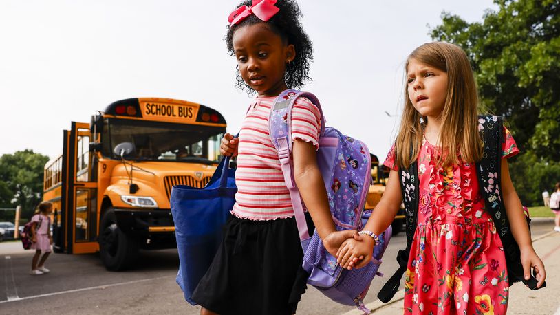 First graders Giana Brito, left, and Feyre Gross hold hands as they get off the bus for the first day of school at Fairfield South Elementary Thursday, Aug. 8, 2024 in Fairfield. NICK GRAHAM/STAFF