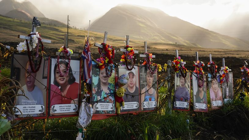 FILE - Photos of victims are displayed under white crosses at a memorial for victims of the August 2023 wildfire, above the Lahaina Bypass highway, Dec. 6, 2023, in Lahaina, Hawaii. (AP Photo/Lindsey Wasson, File)