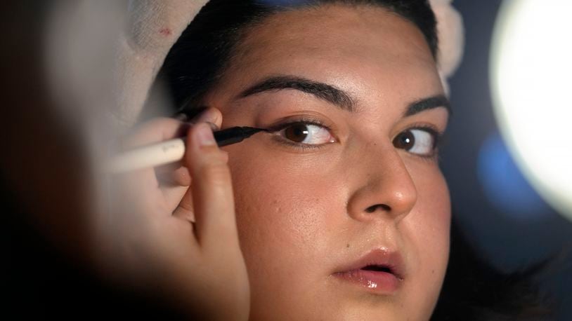 Daniella López White, of Hawaii, uses a mirror while applying makeup, Tuesday, May 14, 2024, at her apartment in Boston. López White, who graduated from Emerson College in Boston this month and is on a tight budget, said TikTok influencers have helped her with tips on how to find affordable clothes at places like H&M and thrift shops. She buys makeup brands at CVS based on influencer advice. (AP Photo/Steven Senne)