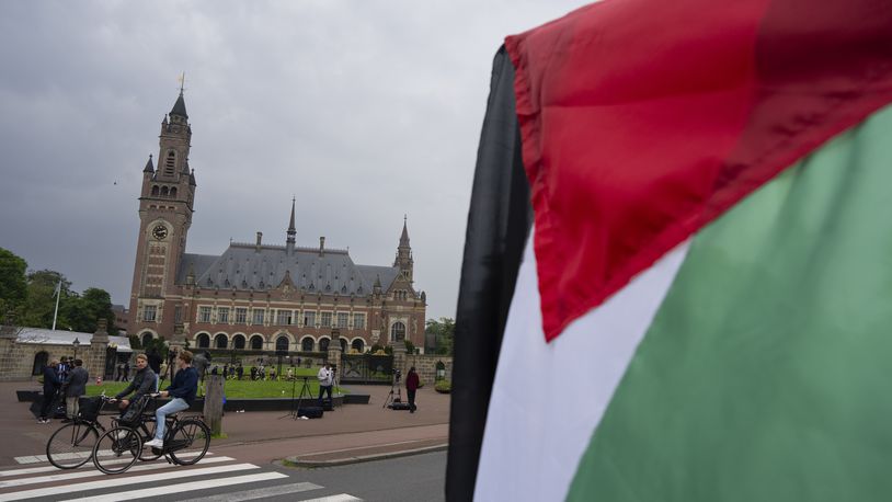 A lone demonstrator waves the Palestinian flag outside the Peace Palace, rear, housing the International Court of Justice, or World Court, in The Hague, Netherlands, Friday, May 24, 2024. The top United Nations court was to rule on an urgent plea by South Africa for judges to order Israel to halt its military operations in Gaza and withdraw from the enclave. (AP Photo/Peter Dejong)