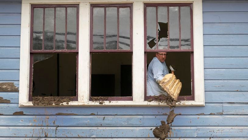 Ben Phillips scoops mud out a window of his house left in the wake of Hurricane Helene, Tuesday, Oct. 1, 2024, in Marshall, N.C. (AP Photo/Jeff Roberson)