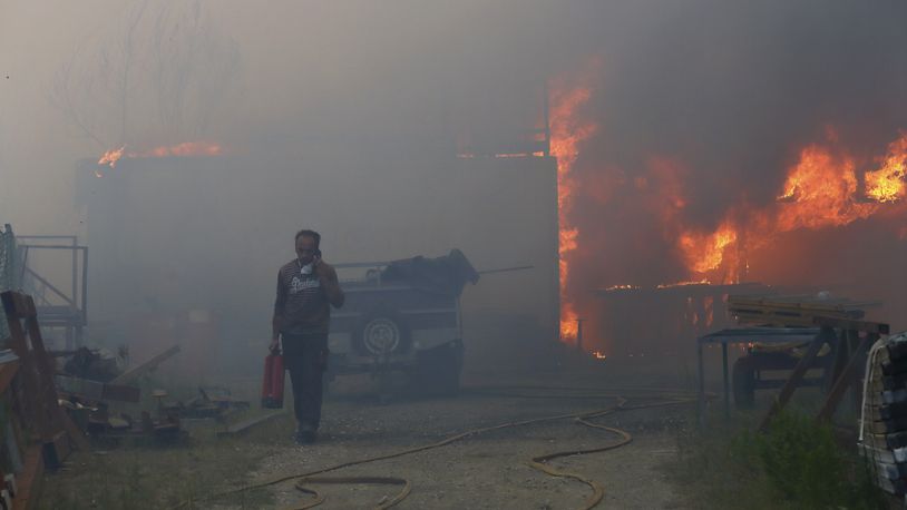 A man carries a fire extinguisher and seeks on the phone while a metalworking warehouse burns in Sever do Vouga, a town in northern Portugal that has been surrounded by forest fires, Monday, Sept. 16, 2024. (AP Photo/Bruno Fonseca)