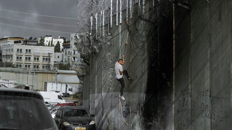 A Palestinian man climbs the separation wall at the town of al-Ram to illegally cross into Jerusalem, Sunday, Sept. 15, 2024. (AP Photo/Mahmoud Illean)