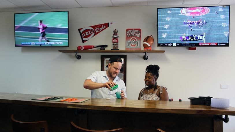 Brenton Semplak, from the Waterford's therapy team, served as bar tender for the grand opening of the sports bar at the Waterford of Fairfield. Activities director Alexis Jenkins was one of many served by Semplak. Sue Kiesewetter/for the Journal-News