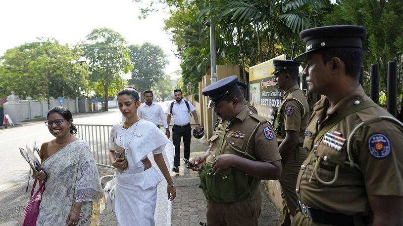 Women election officials walk past security personnel outside a distribution center before collecting polling materials for the upcoming presidential election, in Colombo, Sri Lanka, Friday, Sept. 20, 2024. (AP Photo/Eranga Jayawardena)