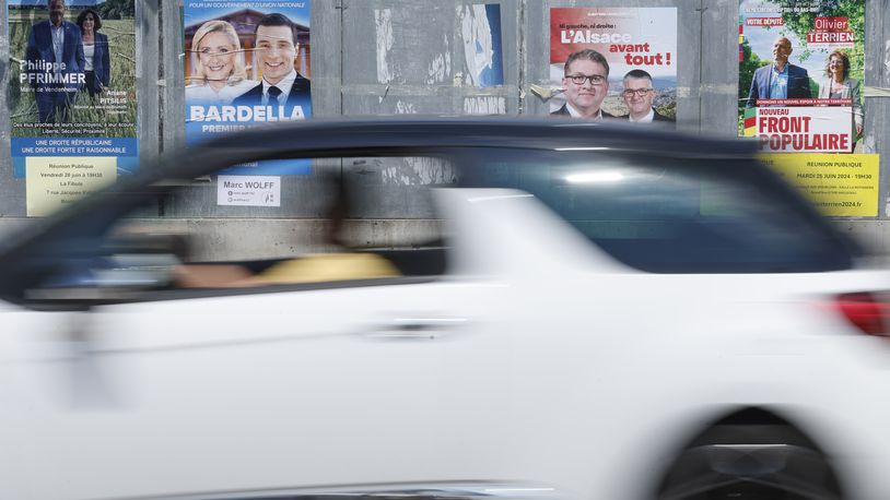 A car drives past electoral posters, Thursday, June 27, 2024 in Strasbourg, eastern France. French President Emmanuel Macron called snap elections following the defeat of his centrist alliance at European Union elections earlier this month. Voters will choose lawmakers for the National Assembly in two rounds on June 30 and July 7. (AP Photo/Jean-Francois Badias)