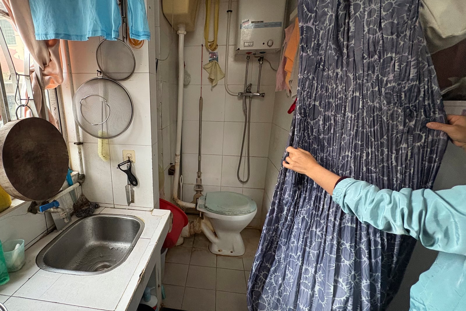 Housewife Jimmy Au pulls back a curtain to reveal her toilet at home in a residential area of Prince Edward district in Hong Kong, on Jan. 21, 2025. (AP Photo/Kanis Leung)