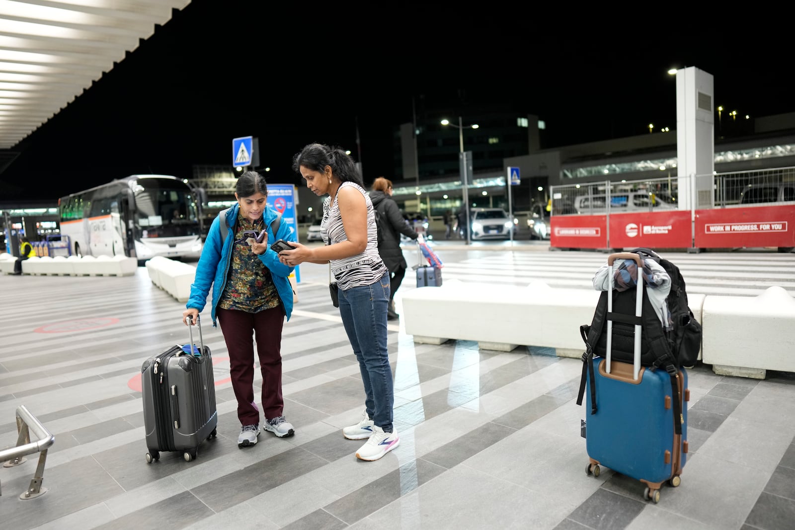 Kavitha Sashi Kumar, right, and Sumana Gheta, both from Dallas, TX, and passengers of American Airlines flight AA292 en route from New York to New Delhi that turned around over the Caspian Sea Sunday, Feb. 23, 2025, and landed at Rome's Leonardo da Vinci International airport check their phones. (AP Photo/Bernat Armangue)