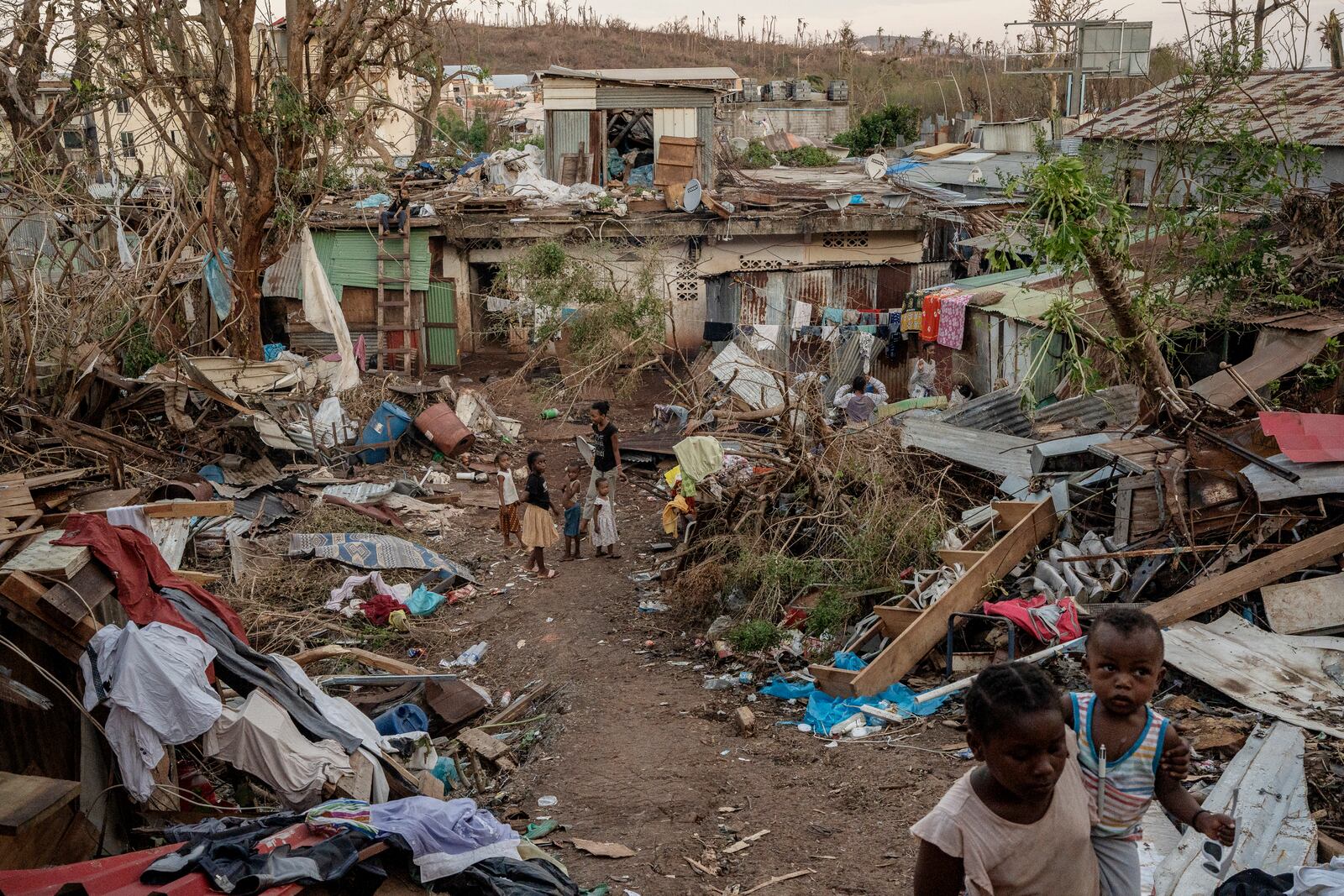 A family stands in the middle of wreaked houses in Mamoudzou, Mayotte, Thursday, Dec. 19, 2024 (AP Photo/Adrienne Surprenant)