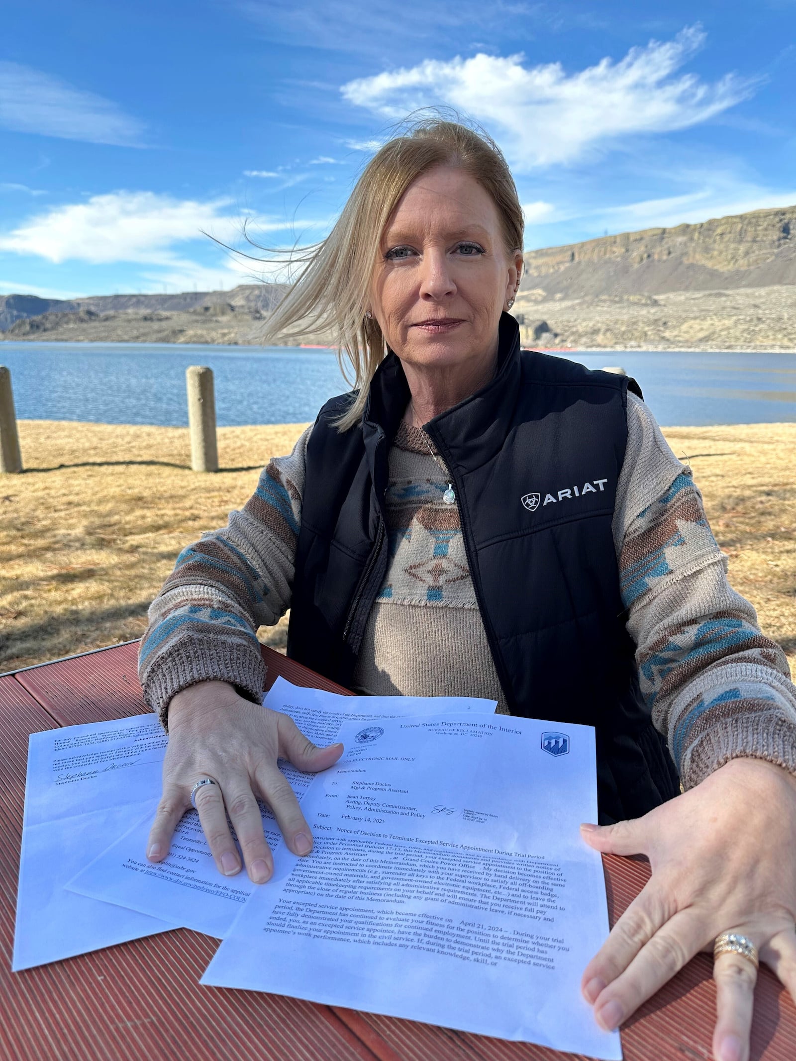 Former Grand Coulee Dam worker, Stephanie Duclos, sits at a picnic table in front of Banks Lake in Electric City, Wash., holding a letter from the Department of Interior, Bureau of Reclamation on Friday, Feb. 28, 2025, saying she has been terminated from her job. (AP Photo/Martha Bellisle)