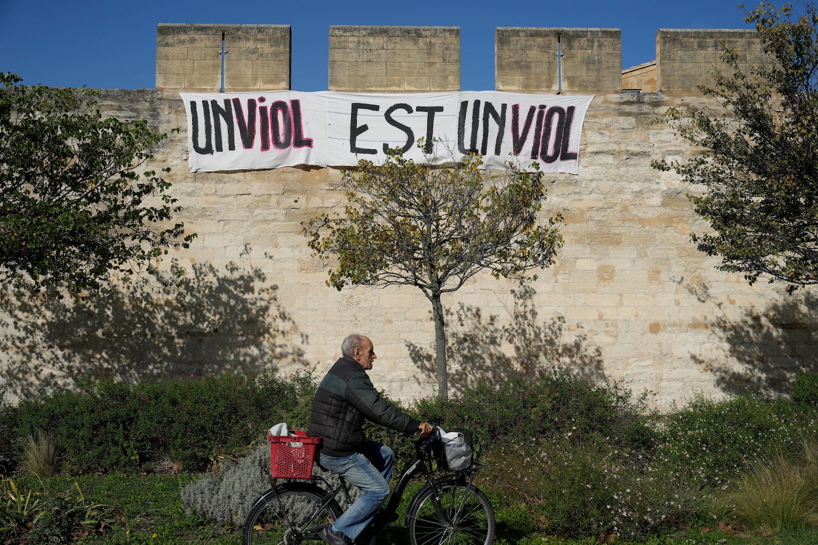 FILE - A man rides a bicycle in front of a banner that reads, "A rape is a rape," in Avignon, southern France, on Oct. 16, 2024. (AP Photo/Lewis Joly, File)