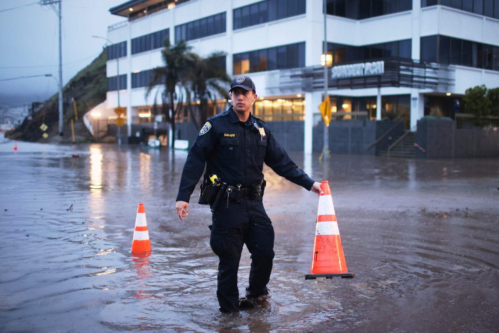 A police officer stands in a flooded intersection during a storm Thursday, Feb. 13, 2025, in the Pacific Palisades neighborhood of Los Angeles. (AP Photo/Ethan Swope)