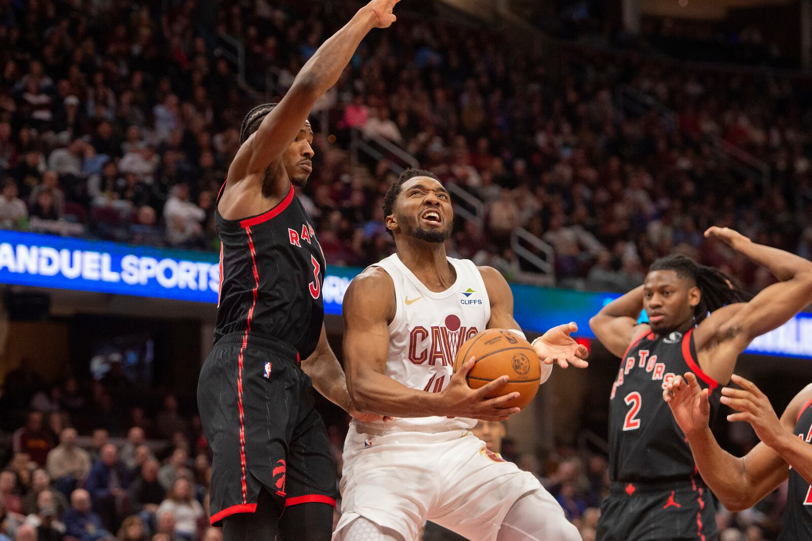 Cleveland Cavaliers' Donovan Mitchell, center, drives between Toronto Raptors' Ochai Agbaji, left, and Jonathan Mogbo (2) during the second half of an NBA basketball game in Cleveland, Sunday, Nov 24, 2024. (AP Photo/Phil Long)