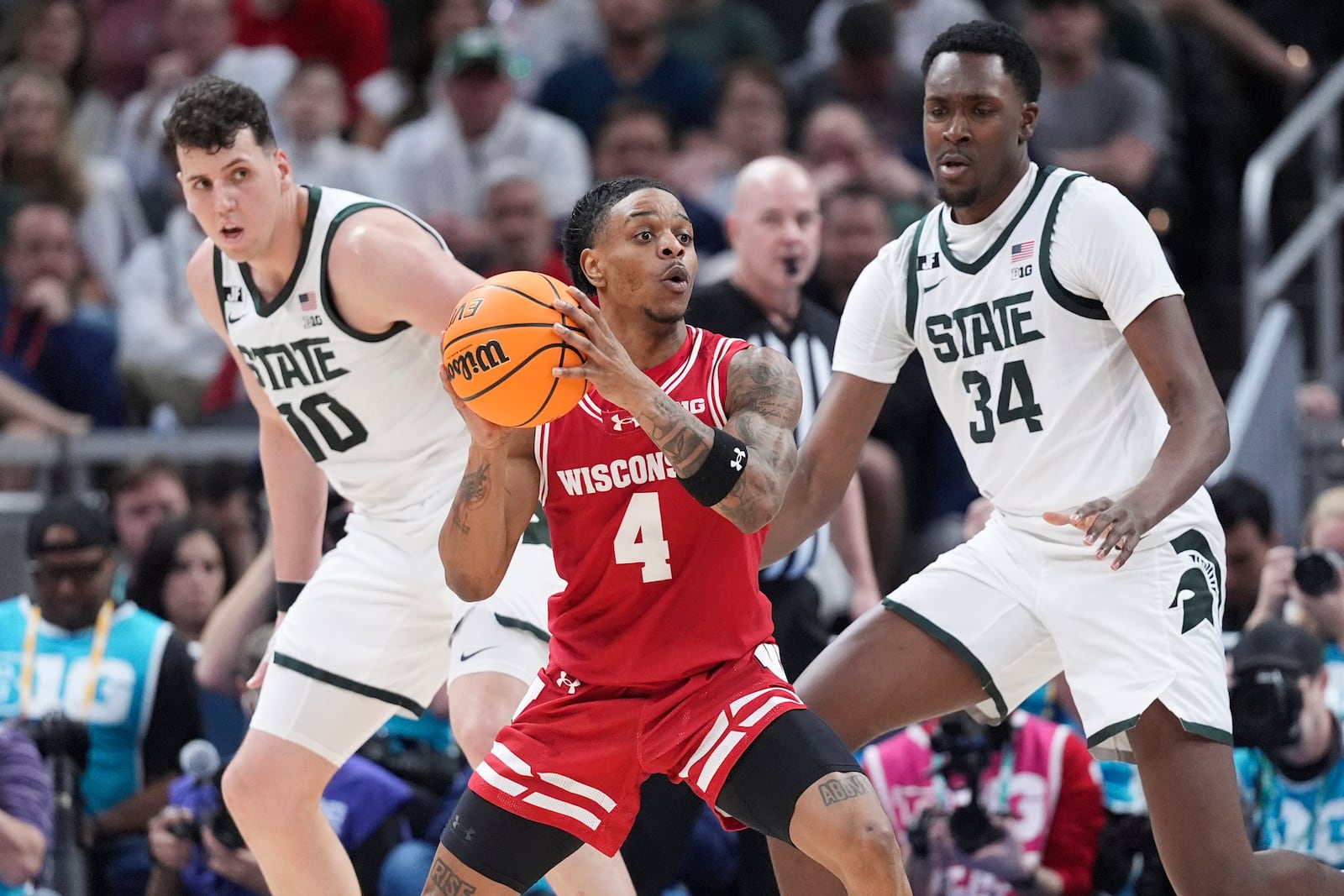 Wisconsin guard Kamari McGee (4) looks to pass as Michigan State center Szymon Zapala (10) and Xavier Booker (34) defend during the first half of an NCAA college basketball game in the semifinals of the Big Ten Conference tournament in Indianapolis, Saturday, March 15, 2025. (AP Photo/Michael Conroy)