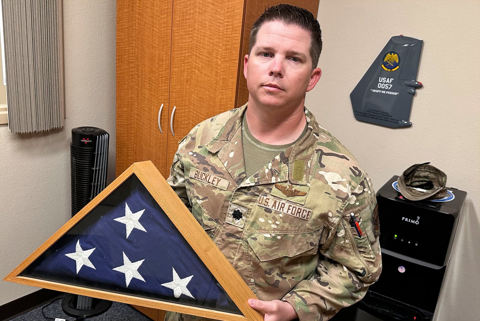 Lt. Col. Seth Buckley, an Osprey squadron commander at Cannon Air Force Base, N.M., who lost his brother in an Air Force Special Operations Command MC-130H crash (AFSOC) when he was still in high school, poses for a photo in his office Oct. 8, 2024.. Buckley says, "I think my job here is to ensure that I'm going to push it to the level that we are making sure we aren't delivering any more of these," he said of the flag the Air Force gave his family, which he keeps in his office. (AP Photo/Tara Copp)