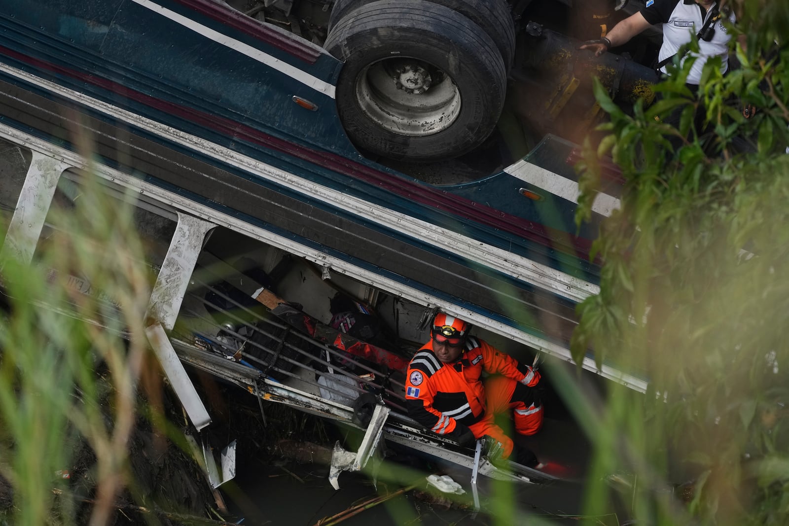 A firefighter works inside a bus that fell from a bridge on the outskirts of Guatemala City, Monday, Feb. 10, 2025. (AP Photo/Moises Castillo)