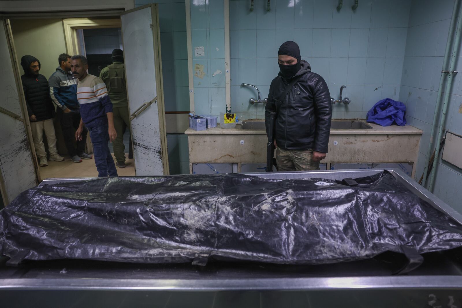 A body lies at the morgue as people stands while waiting to identify missing relatives or friends at the morgue of Al-Mujtahidh in Damascus, Syria, Tuesday, Dec. 10, 2024. (AP Photo/Ghaith Alsayed)