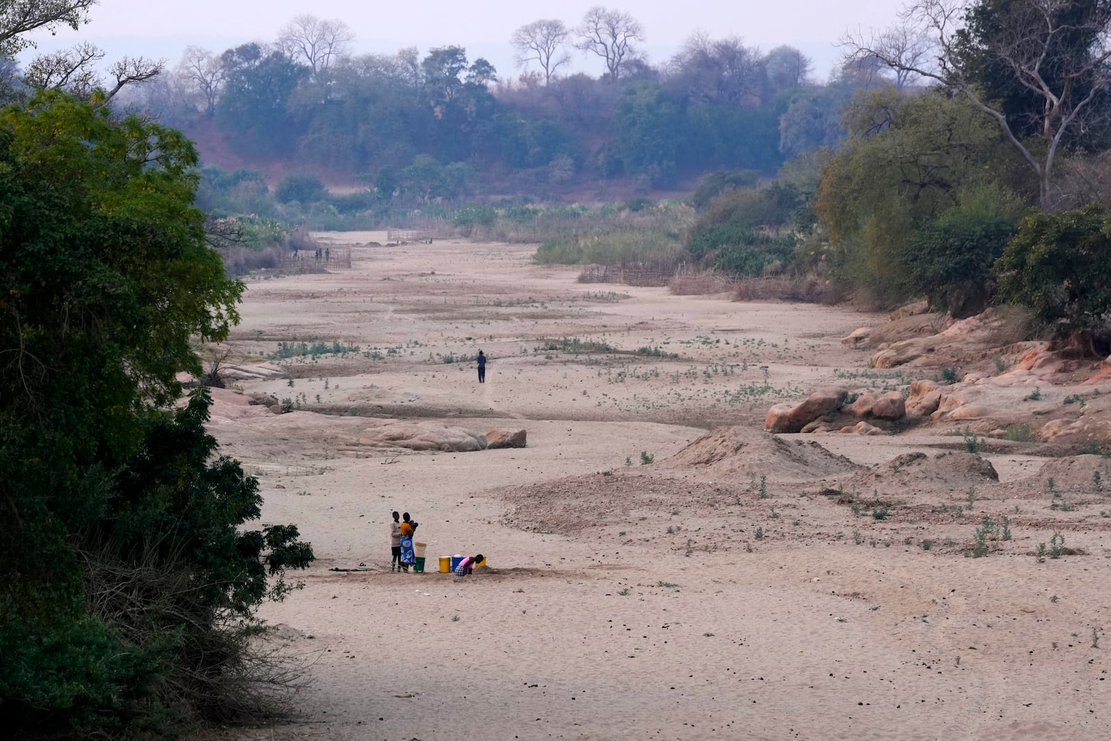 File — A women scoops water from a hole she has dug in a dried up riverbed in Lusitu, Zambia, Wednesday, Sept. 18, 2024. (AP Photo/Themba Hadebe/File)