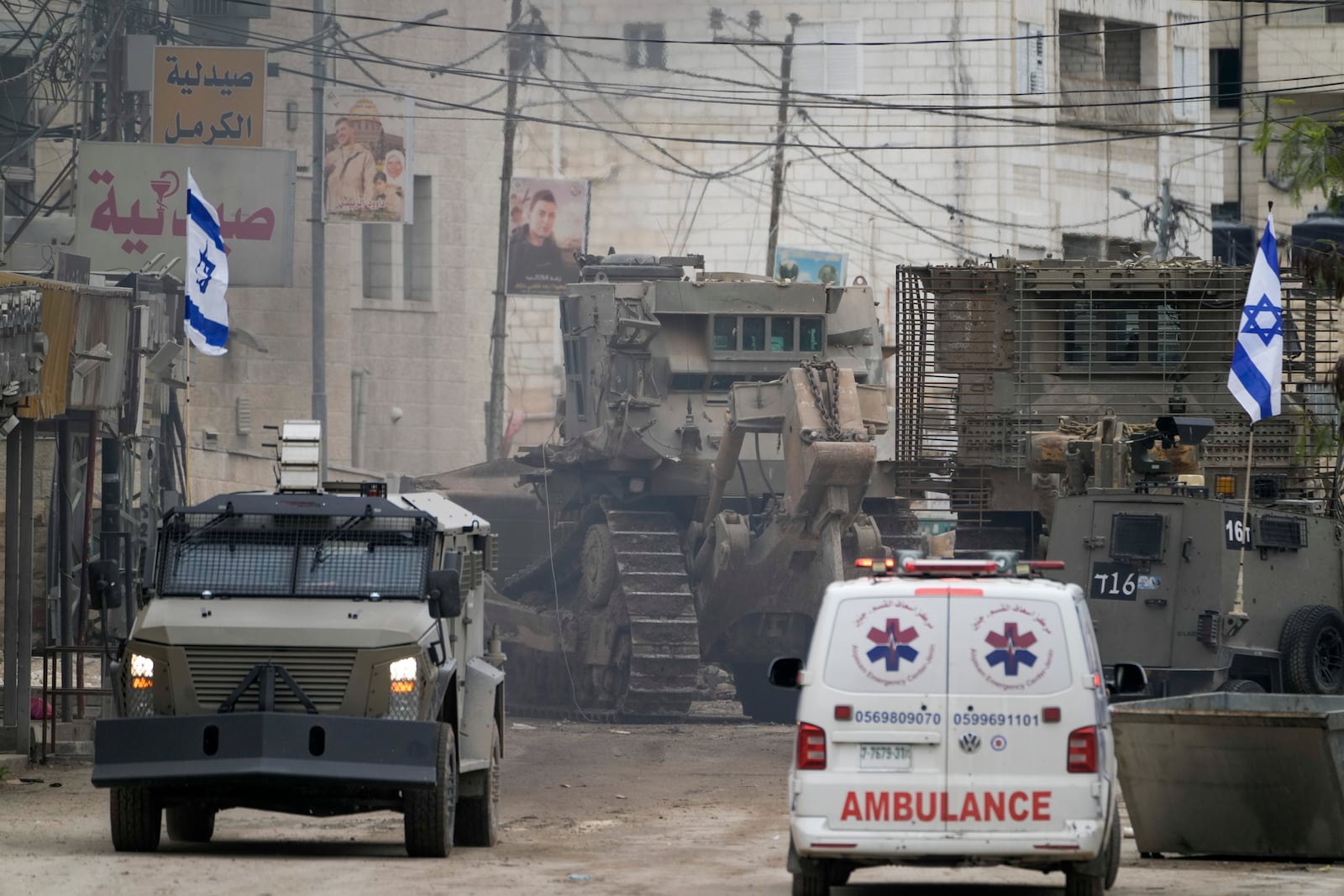 Israeli military vehicles guard a road where a military bulldozer operates in the West Bank refugee camp of Jenin, Wednesday, Jan. 22, 2025. (AP Photo/Majdi Mohammed)