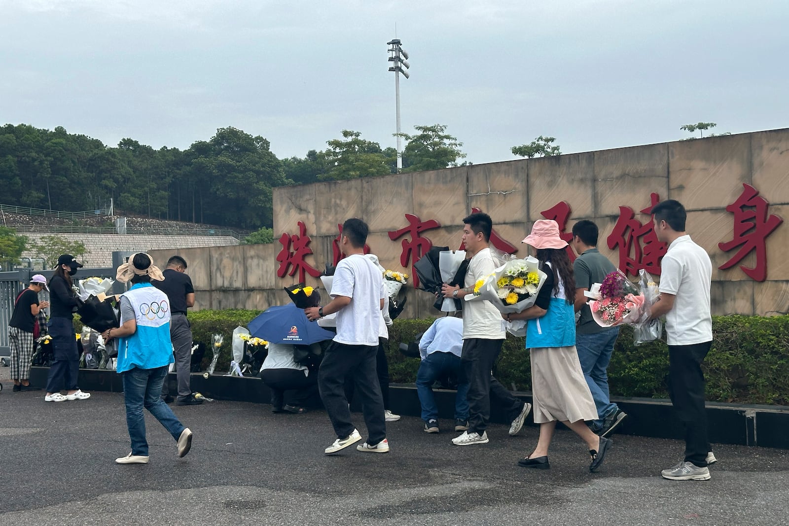 Volunteers relocate flowers laid outside the "Zhuhai People's Fitness Plaza" to a barrier leading into the area where a man rammed his car into people exercising at the sports center, in Zhuhai in southern China's Guangdong province on Wednesday, Nov. 13, 2024. (AP Photo/Ng Han Guan)