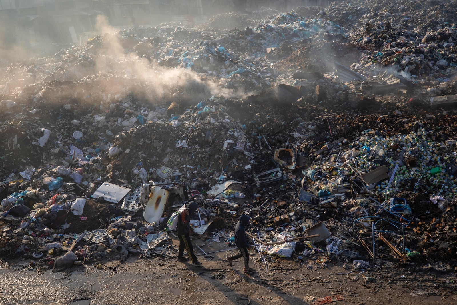 Palestinians walk past a pile of burning garbage, as there is no refuse collection in the city and people are disposing of their rubbish in the streets, in Gaza City, Wednesday, Feb. 12, 2025. (AP Photo/Jehad Alshrafi)