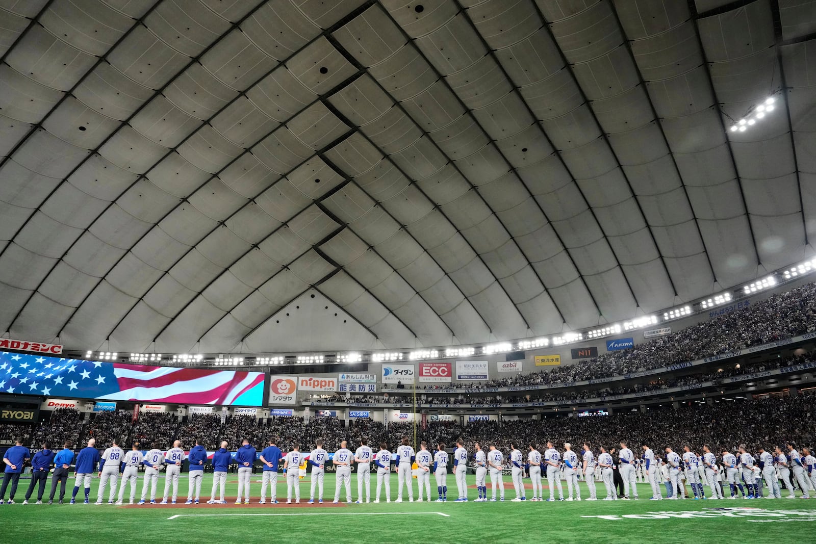 The Los Angeles Dodgers line up on the field during the playing of the national anthem before their MLB Japan Series baseball game against the Chicago Cubs in the Tokyo Dome in Tokyo, Japan, Tuesday, March 18, 2025. (AP Photo/Eugene Hoshiko)