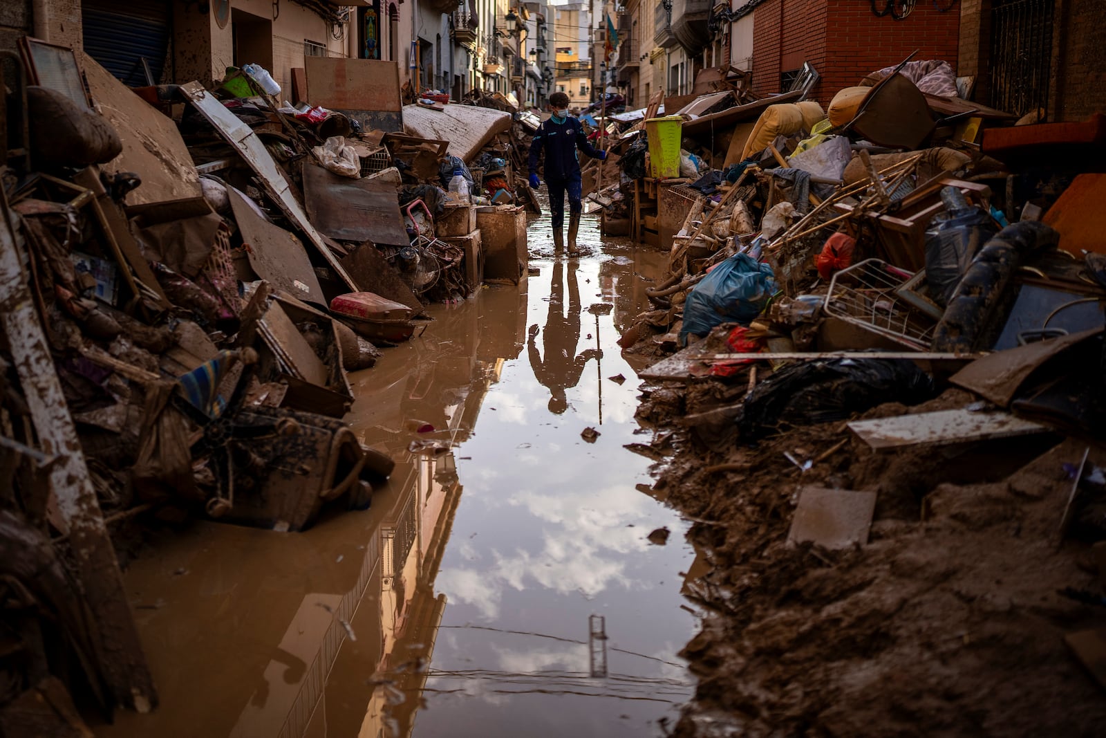 A person walks through a street with piled furniture and rubbish on the sides in an area affected by floods in Paiporta, Valencia, Spain, Tuesday, Nov. 5, 2024. (AP Photo/Emilio Morenatti)