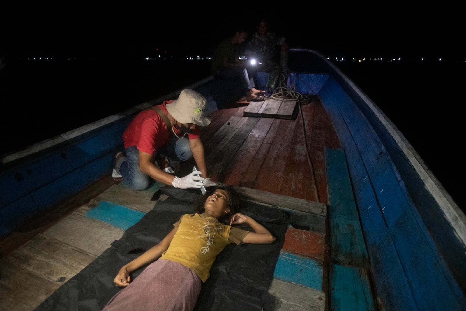 A paramedic examines the health condition of young girl as she lies on the deck of a boat carrying Rohingya Muslims in the waters near the coast of Labuhan Haji, Aceh province, Indonesia, Tuesday, Oct. 22, 2024. (AP Photo/Binsar Bakkara)