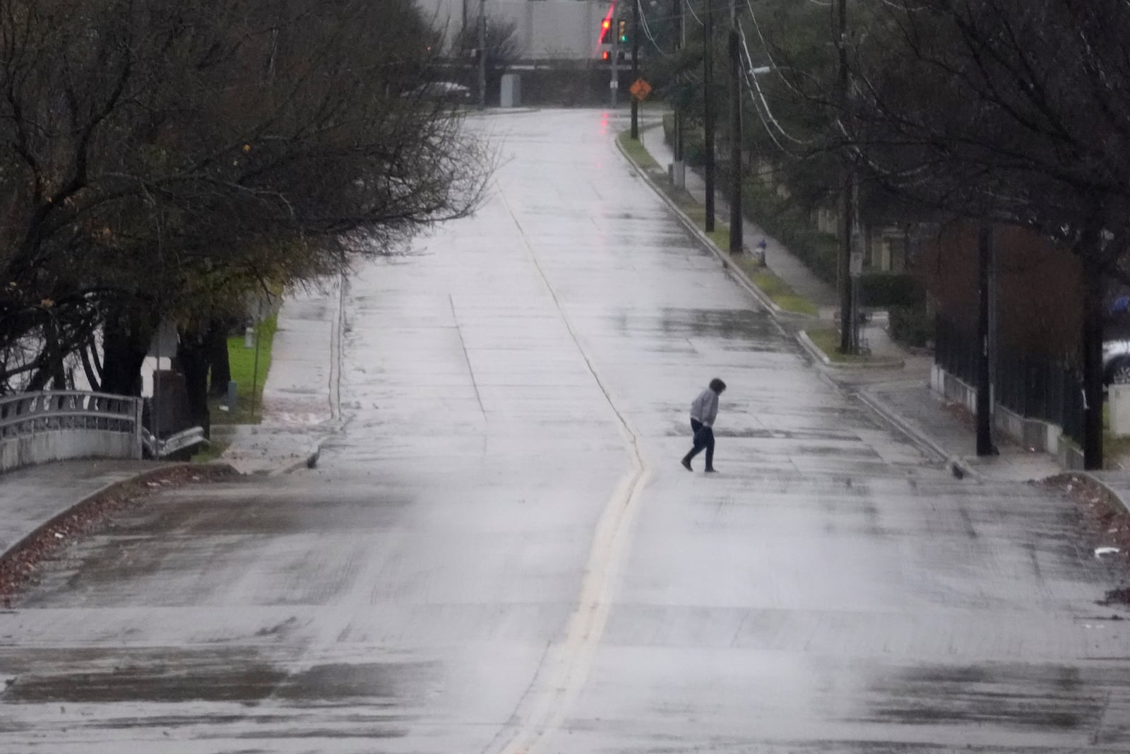 A pedistrian walks across a rain soaked street in Dallas, Thursday, Dec. 26, 2024. (AP Photo/LM Otero)