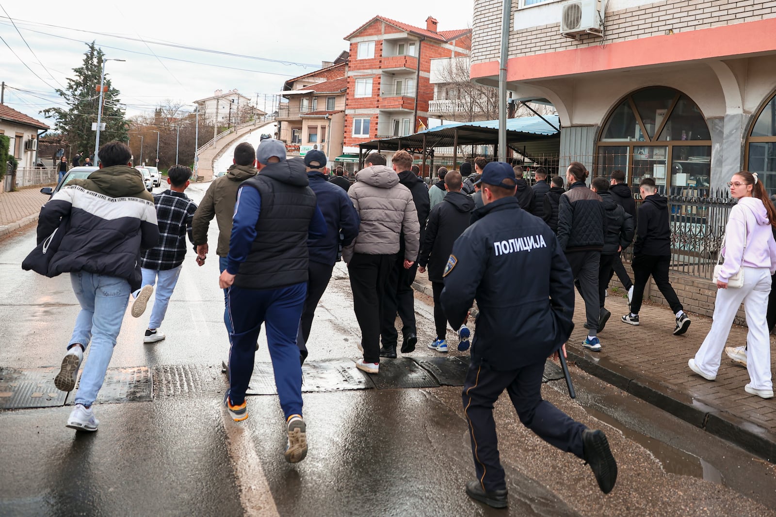 A policeman runs behind people heading to the home of the owner of a nightclub that was the scene of a massive fire, after a vigil for the victims in the town of Kocani, North Macedonia, Monday, March 17, 2025. (AP Photo/Armin Durgut)