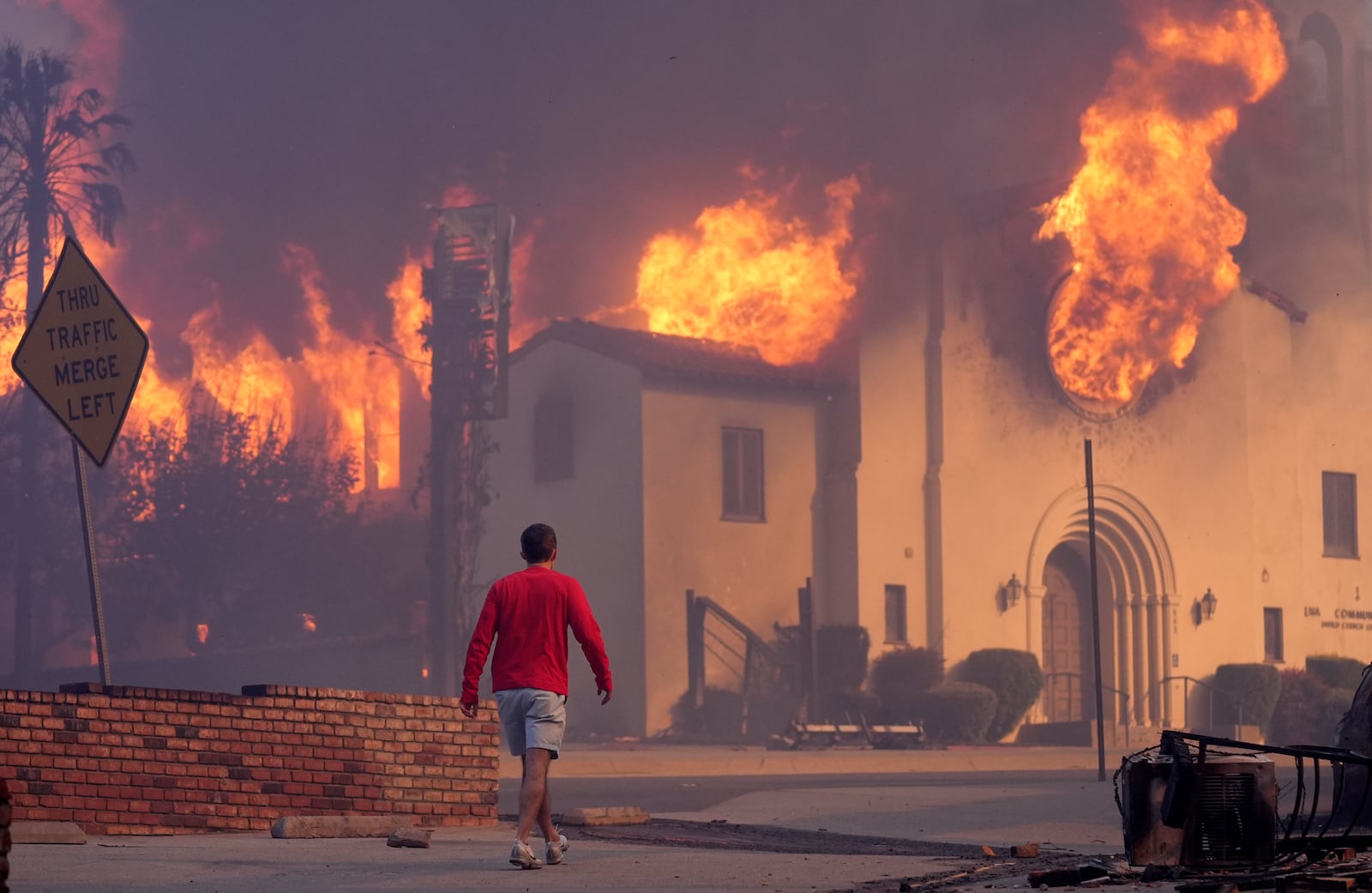 A man walks in front of the burning Altadena Community Church, Wednesday, Jan. 8, 2025, in the downtown Altadena section of Pasadena, Calif. (AP Photo/Chris Pizzello)