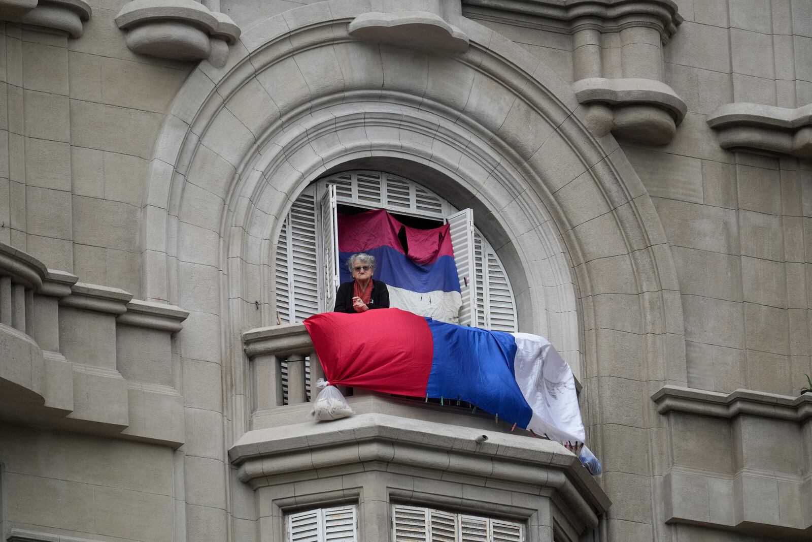 A woman stands on a balcony looking out at people gathering in Independent Square where President-elect Yamandu Orsi will receive the presidential sash, on Inauguration Day in Montevideo, Uruguay, Saturday, March 1, 2025. (AP Photo/Matilde Campodonico)