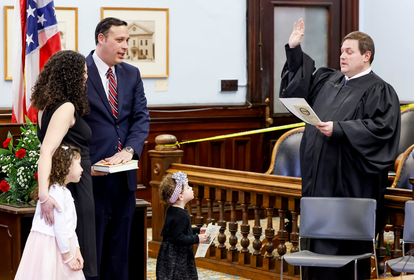 Daniel Phillips, with his wife, Sarah, and daughters, Ellie, 5, and Sophie, 2, is sworn in by Butler County Common Pleas Court Judge Daniel Haughey, right, as Butler County Juvenile Court Judge Thursday, Dec. 29, 2022 at the historic Butler County Courthouse in Hamilton. NICK GRAHAM/STAFF