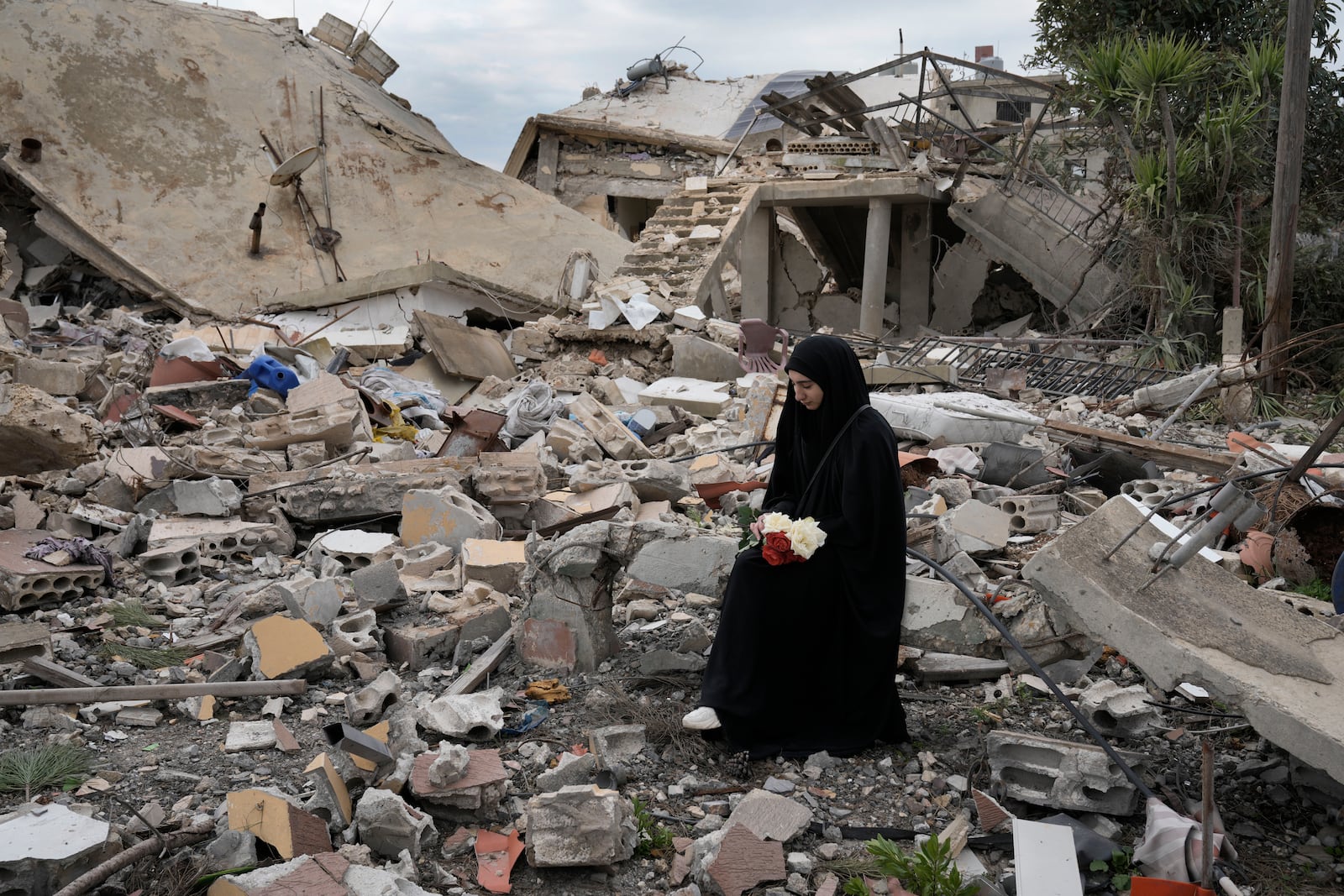 A Lebanese woman holds a bouquet of flowers, as she sits on the rubble of a destroyed house caused by the Israeli air and ground offensive, in Aita al-Shaab, a Lebanese border village with Israel, south Lebanon, Sunday, Jan. 26, 2025. (AP Photo/Bilal Hussein)