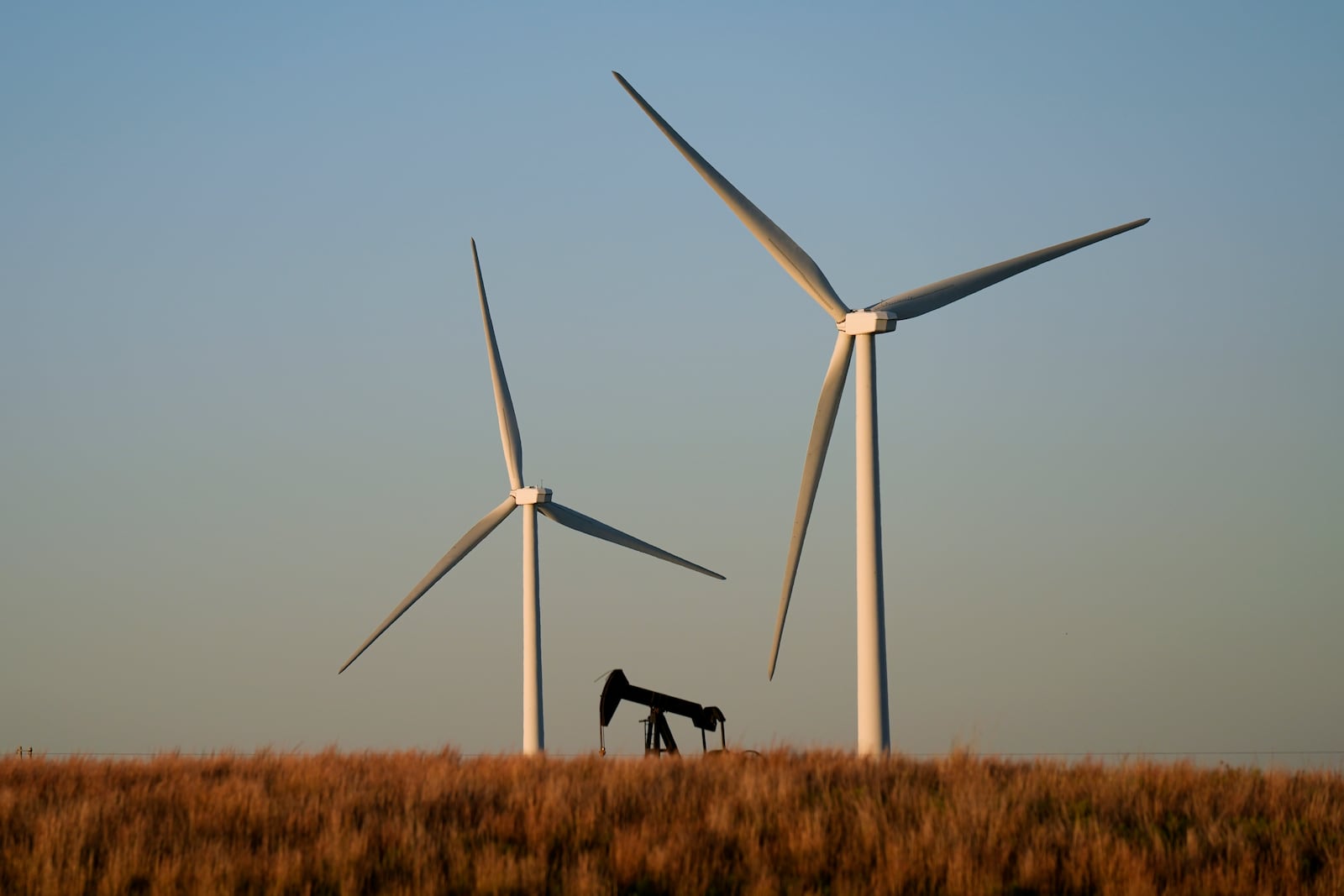 FILE - An oil pumping unit works in the foreground while wind turbines at the Buckeye Wind Energy wind farm rise in the distance Sept. 30, 2024, near Hays, Kan. (AP Photo/Charlie Riedel, File)