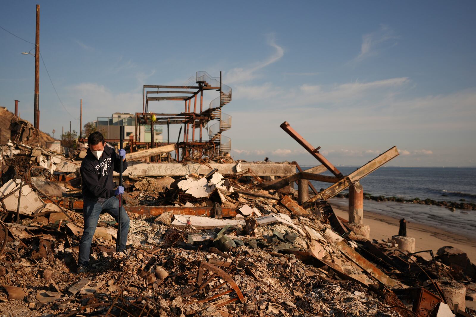 Tony Lai rakes through the remains of his fire-ravaged beachfront property in the aftermath of the Palisades Fire Tuesday, Jan. 28, 2025 in Malibu, Calif. (AP Photo/Jae C. Hong)