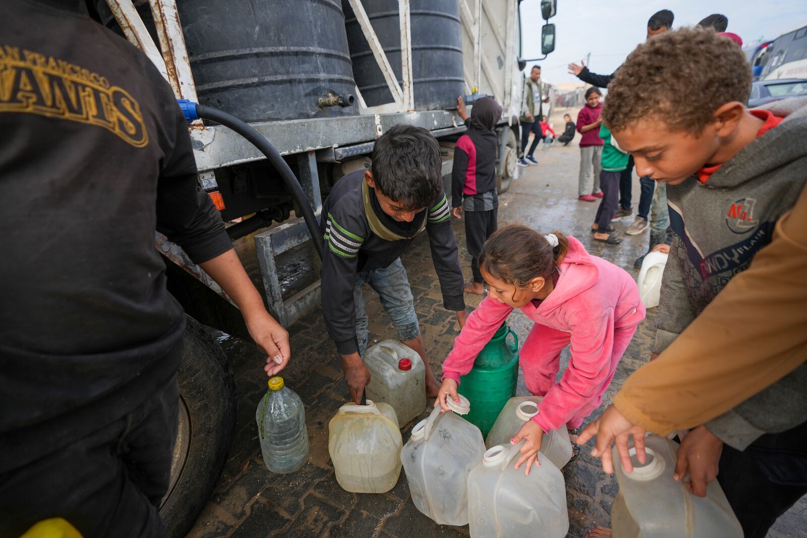 Children collect water from a truck at a tent camp for displaced Palestinians in Deir al-Balah, central Gaza Strip, Thursday Jan. 16, 2025. (AP Photo/Abdel Kareem Hana)