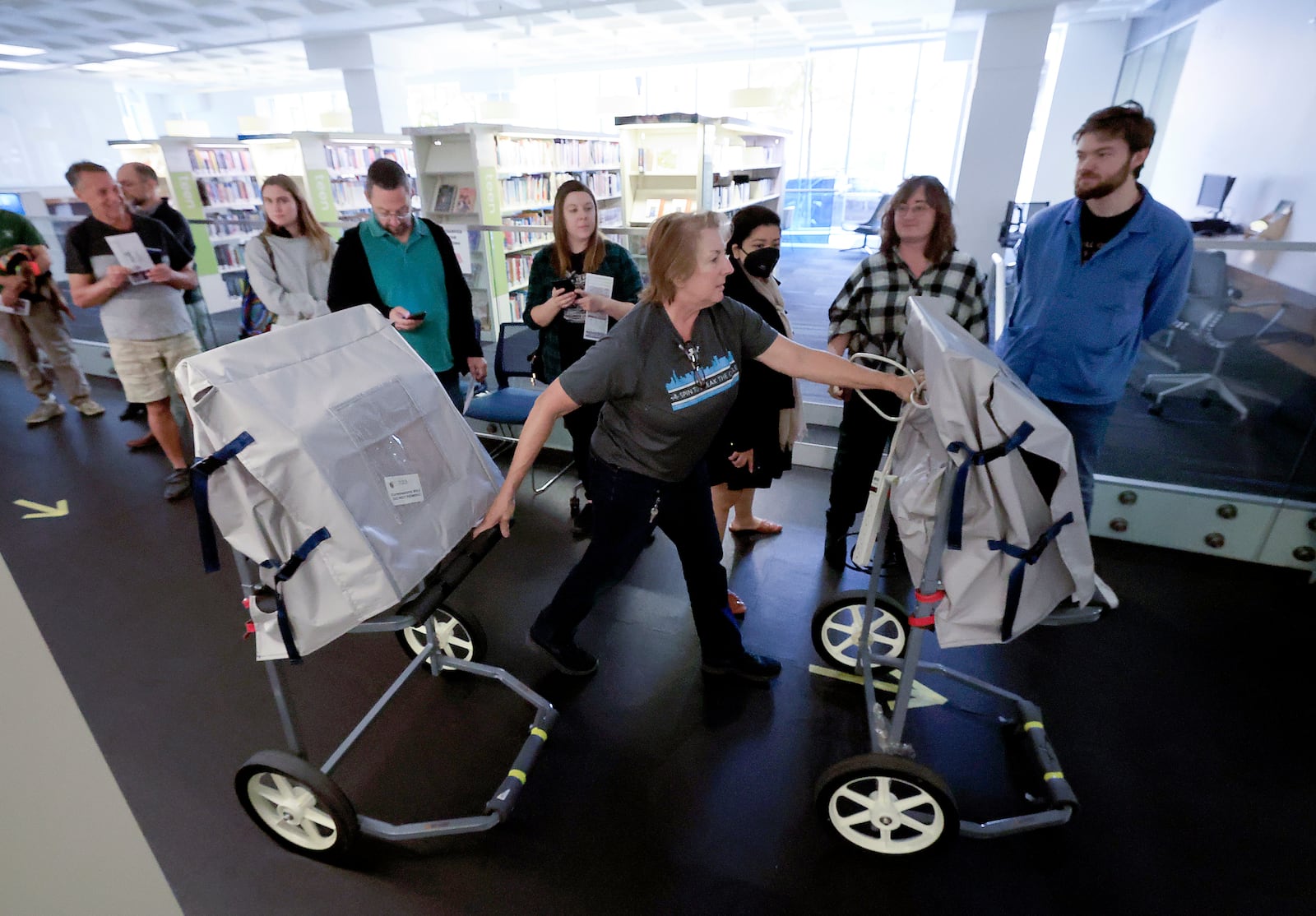 A Madison Clerk's Office worker delivers a pair of additional polling booths past people waiting to vote on the first day of Wisconsin's in-person absentee voting at the Madison Public Library in Madison, Wisc., Tuesday, Oct. 22, 2024. (AP Photo/John Hart, Wisconsin State Journal)