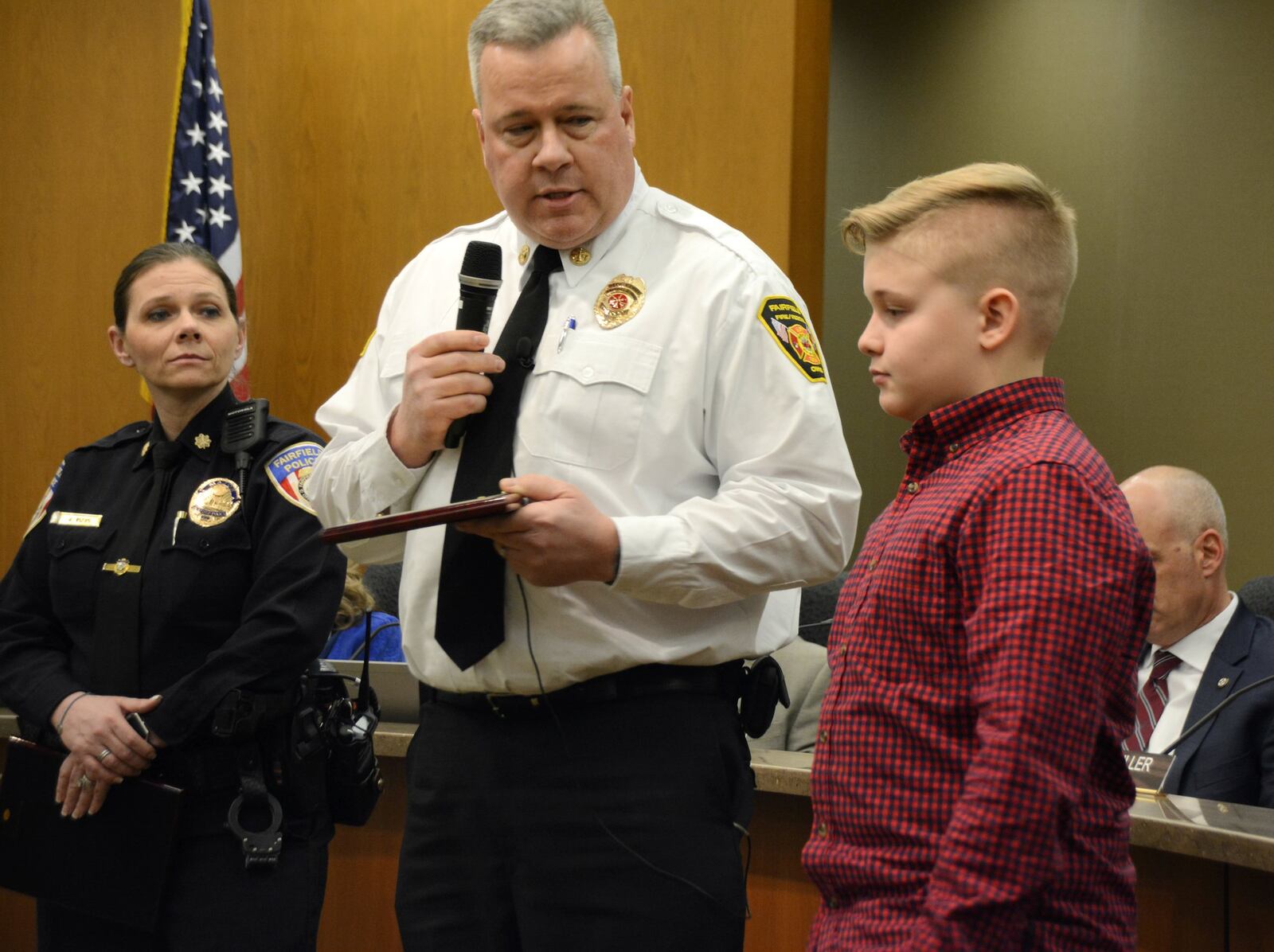 Fairfield Deputy Fire Chief Tom Wagner (center) presents an award of appreciation to Myles Macbeth (right), 13, of River Road, after on Dec. 20, 2018, helped save his grandfather, Ed Hassler, who was profusely bleeding from a head wound caused by a fall. Fairfield Police Major Amy Mays, (left) who oversees the dispatch, watches the presentation. MICHAEL D. PITMAN/STAFF