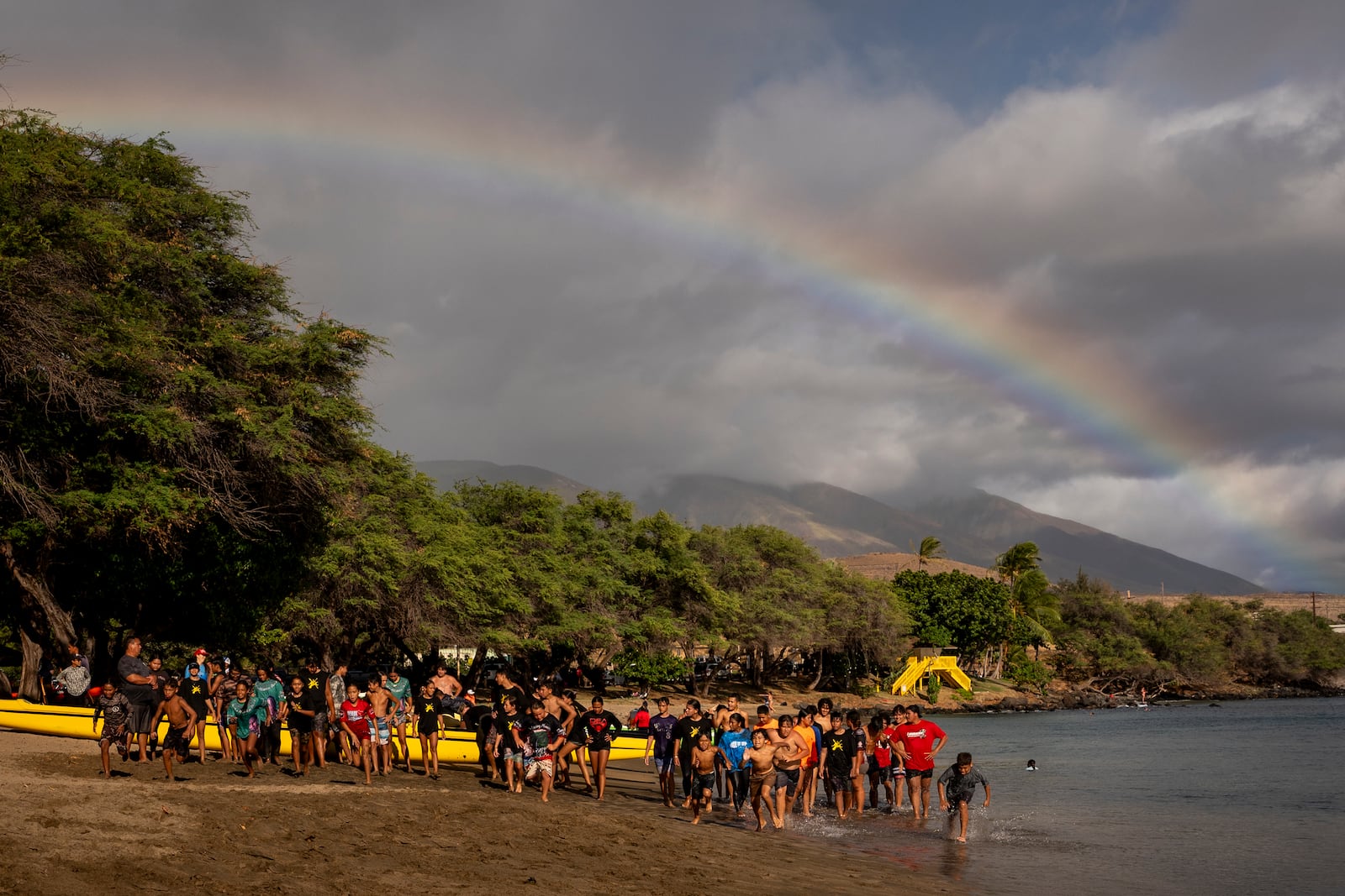 Members of the Napili Canoe Club run sprints on the beach as a rainbow forms nearby on Monday, July 8, 2024, at Hanakao'o Park in Lahaina, Hawaii. (AP Photo/Lindsey Wasson)