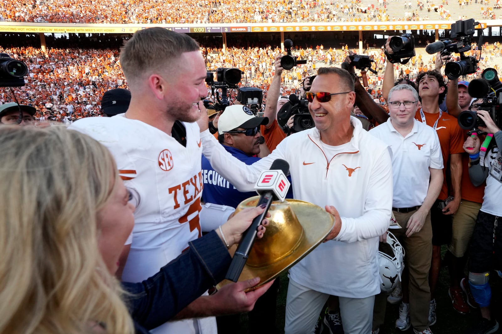 Texas quarterback Quinn Ewers, left, and head coach Steve Sarkisian, center right, hold the Golden Hat Trophy after their team's win against Oklahoma in an NCAA college football game in Dallas, Saturday, Oct. 12, 2024. (AP Photo/Jeffrey McWhorter)