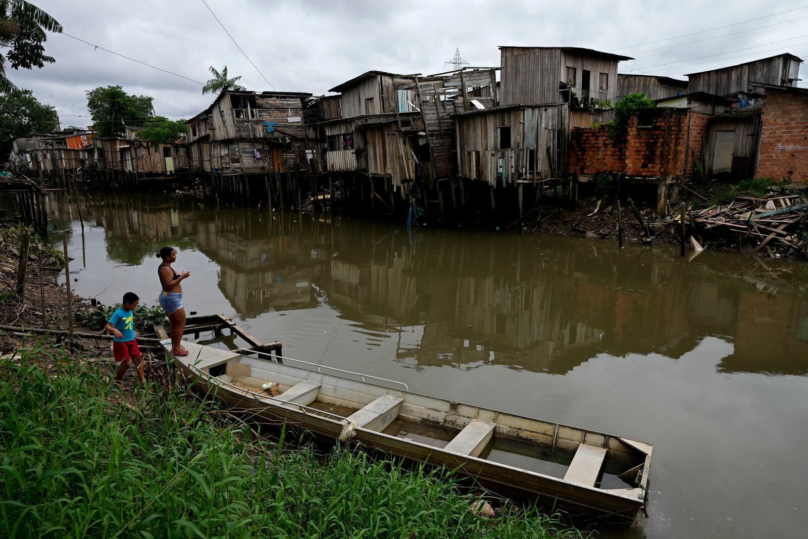 FILE - A mother and son walk on the bank of the Tucunduba Channel where stilt homes stand in the Terra Firme neighborhood of Belem, Brazil, March 26, 2024. (AP Photo/Eraldo Peres, File)