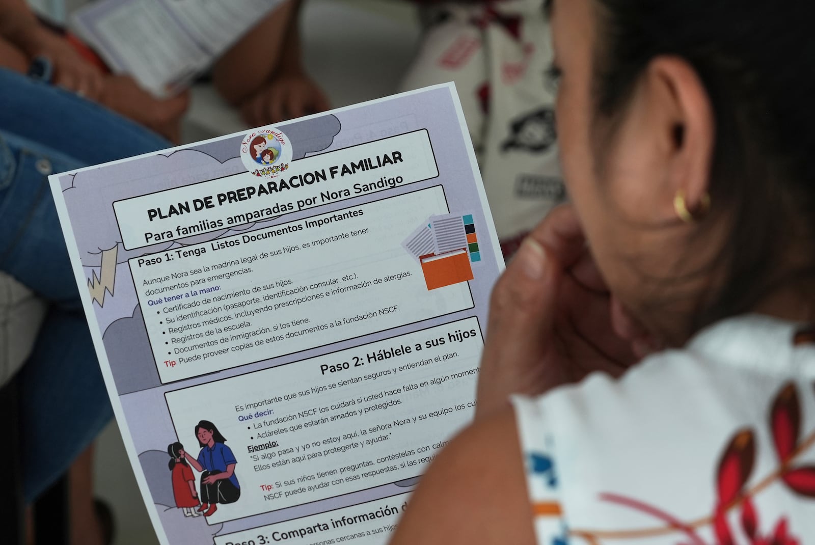 A mother reads a pamphlet to help her family prepare in the event she is apprehended by immigration authorities, Sunday, Jan. 19, 2025, in Miami. (AP Photo/Marta Lavandier)