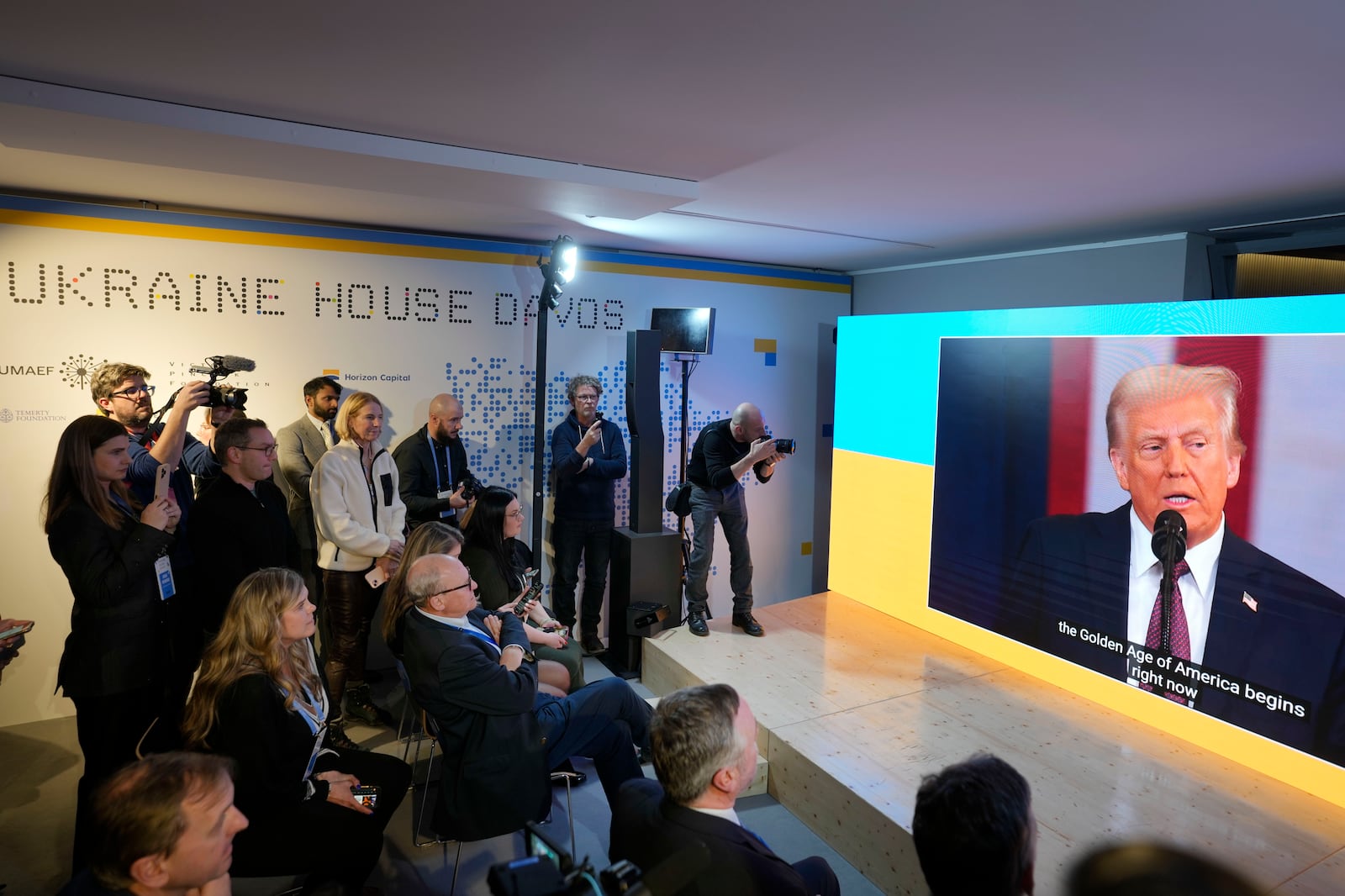 People watch the inauguration speech of Donald Trump on screens at the Ukraine house alongside the World Economic Forum in Davos, Switzerland, Monday, Jan. 20, 2025. (AP Photo/Markus Schreiber)