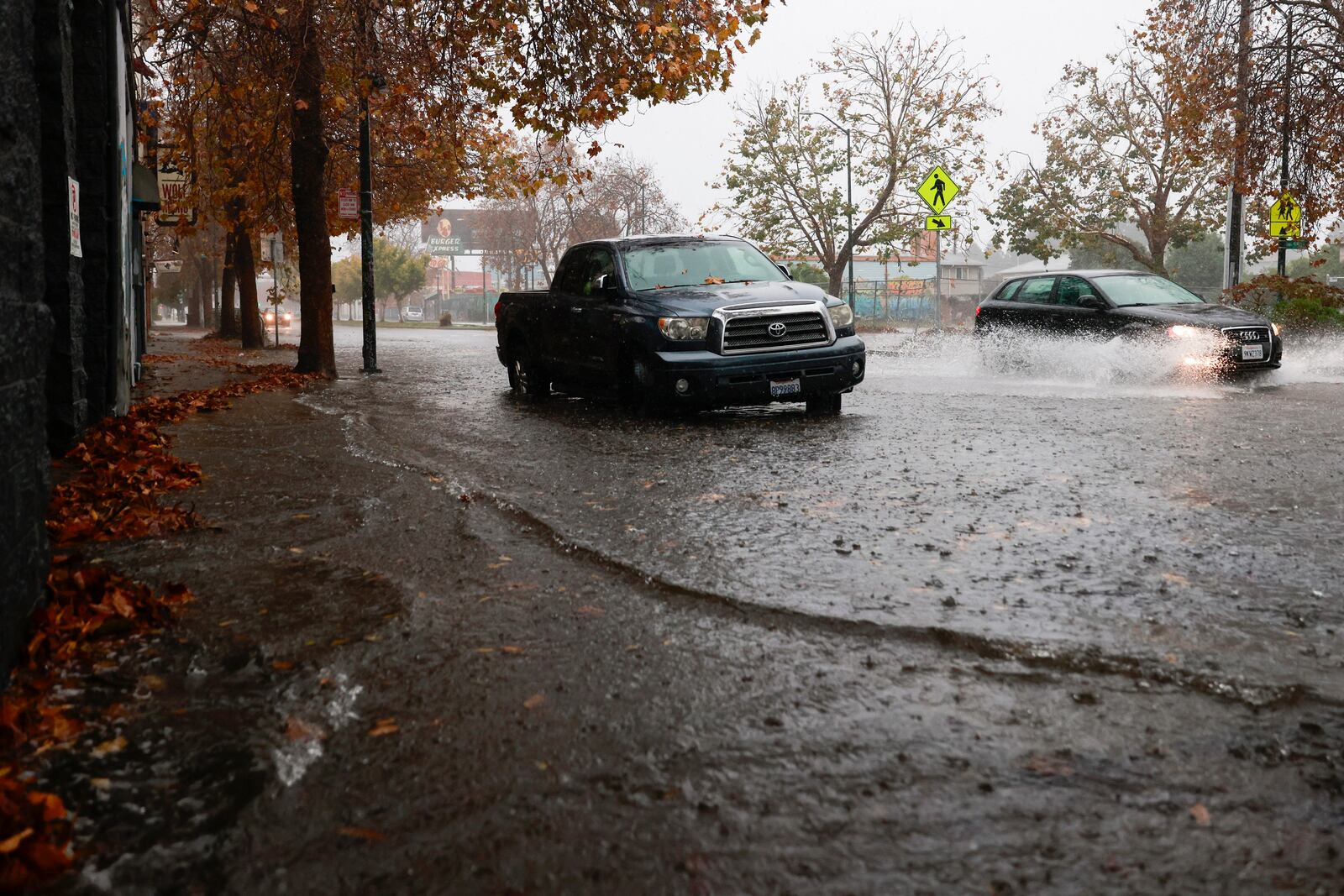 Cars drive through floodwaters as they rise in Oakland, Calif., Friday, Nov. 22, 2024. (Jessica Christian/San Francisco Chronicle via AP)