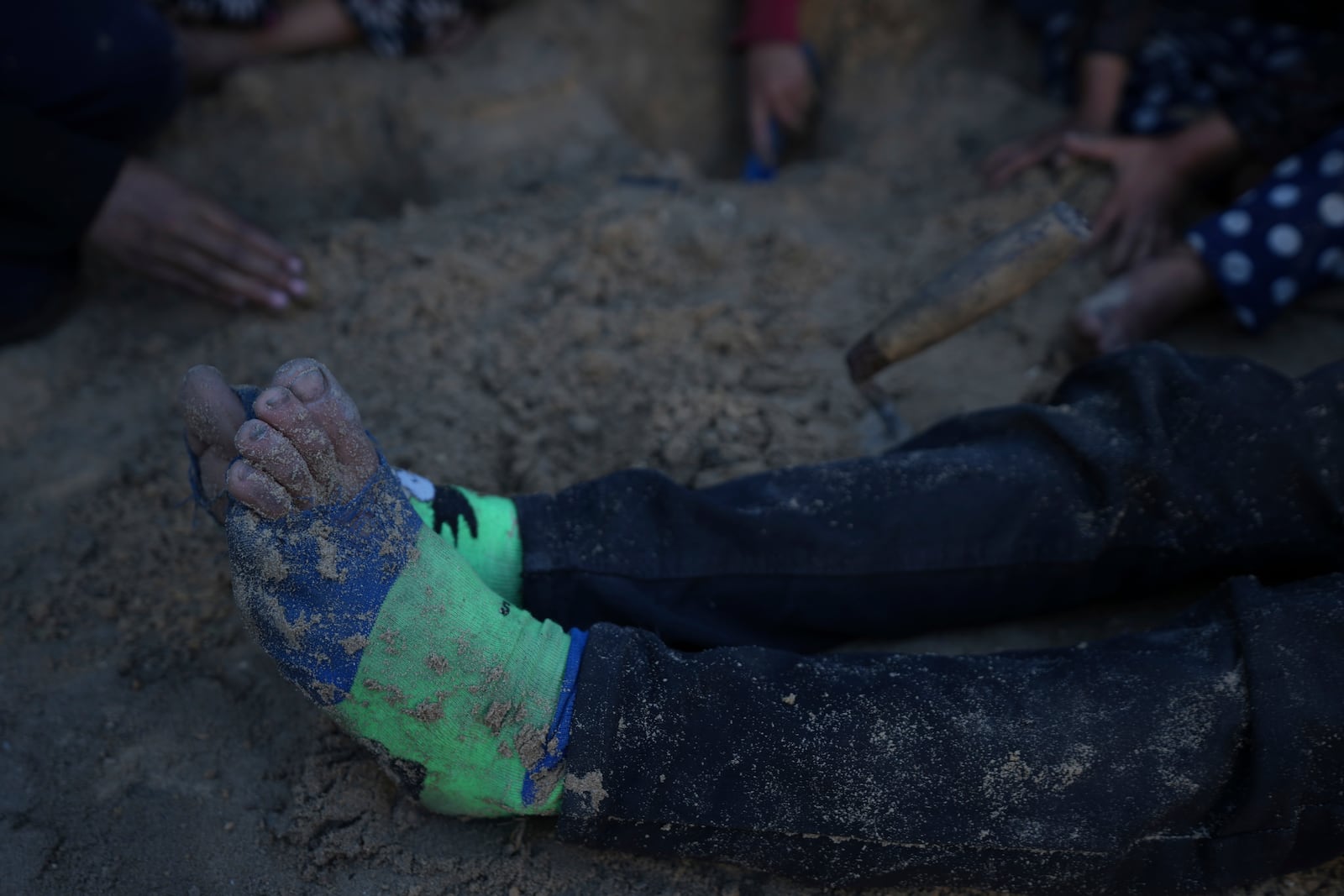 One of Reda Abu Zarada's grandchildren, displaced from Jabaliya in northern Gaza, sits on the dirt wearing torn socks while playing near their tent at a camp in Khan Younis, Gaza Strip, Thursday Dec. 19, 2024. (AP Photo/Abdel Kareem Hana)